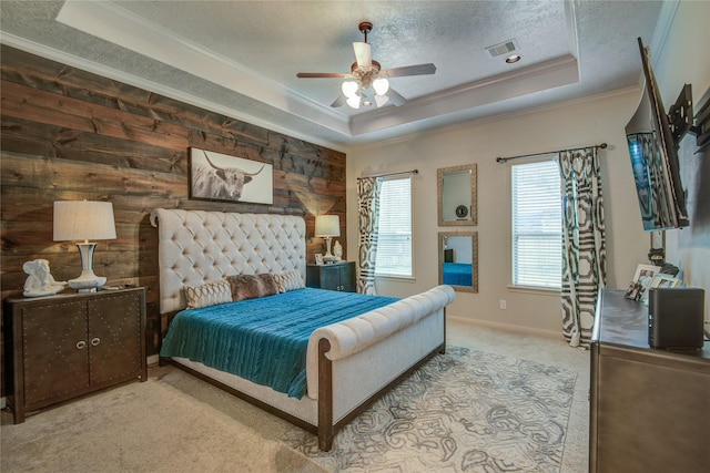 carpeted bedroom with ceiling fan, wooden walls, ornamental molding, a textured ceiling, and a raised ceiling