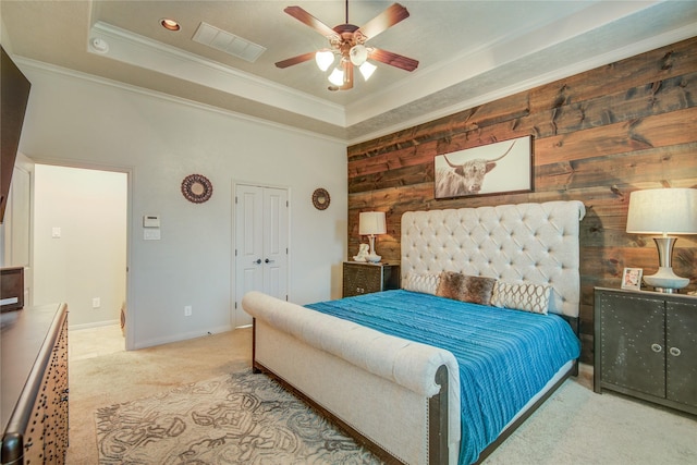 bedroom featuring crown molding, ceiling fan, a tray ceiling, a closet, and wood walls