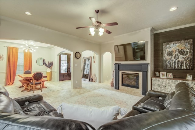 living room with ceiling fan with notable chandelier, ornamental molding, and a tile fireplace