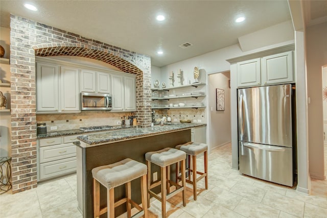 kitchen with dark stone countertops, stainless steel appliances, brick wall, and a kitchen island