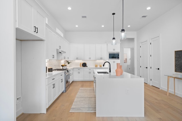 kitchen featuring sink, white cabinetry, hanging light fixtures, stainless steel range with gas stovetop, and an island with sink