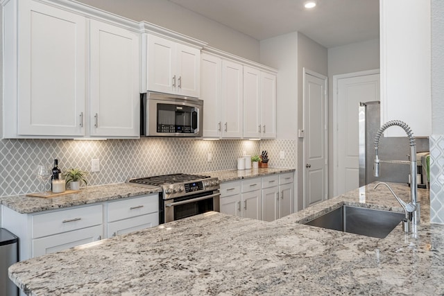 kitchen featuring white cabinetry, appliances with stainless steel finishes, light stone countertops, and sink