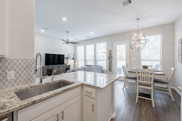 kitchen featuring dark hardwood / wood-style floors, decorative light fixtures, white cabinetry, sink, and light stone countertops