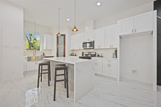 kitchen with sink, white cabinetry, hanging light fixtures, appliances with stainless steel finishes, and a kitchen island