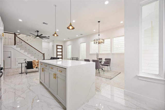 kitchen featuring light stone counters, decorative light fixtures, ceiling fan with notable chandelier, and a kitchen island