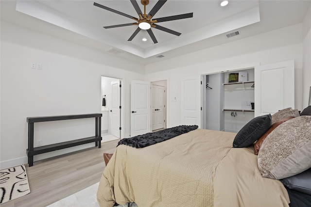 bedroom featuring a raised ceiling, ensuite bathroom, ceiling fan, and light hardwood / wood-style floors