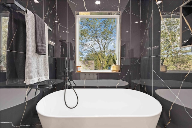 bathroom with a healthy amount of sunlight, a tub to relax in, and tile walls