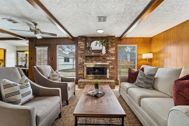 living room with a brick fireplace, beam ceiling, wooden walls, and a textured ceiling