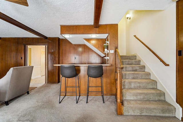 kitchen with beamed ceiling, a breakfast bar, a textured ceiling, and wood walls