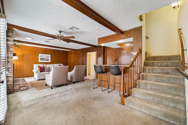 carpeted living room featuring ceiling fan, wooden walls, beam ceiling, and a textured ceiling