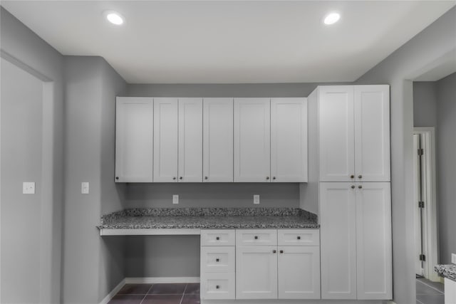 kitchen with light stone counters, dark tile patterned floors, built in desk, and white cabinets