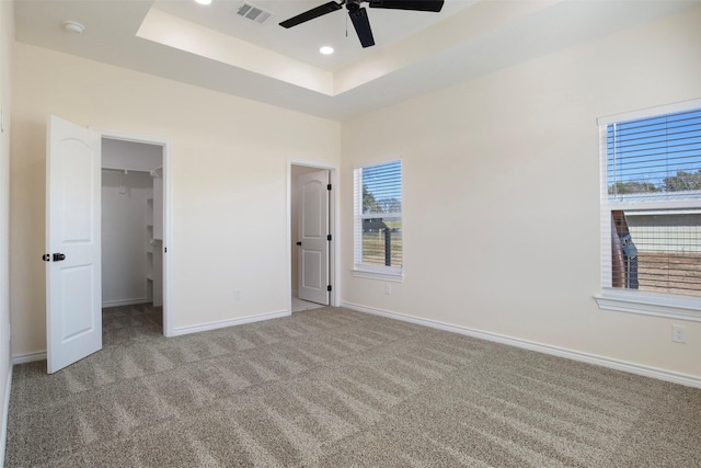 unfurnished bedroom featuring multiple windows, a spacious closet, light colored carpet, and a tray ceiling