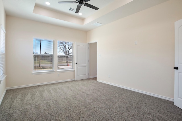 carpeted empty room with a raised ceiling and ceiling fan