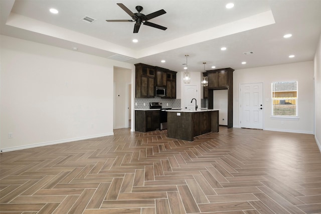 kitchen featuring ceiling fan, stainless steel appliances, dark brown cabinetry, an island with sink, and decorative light fixtures