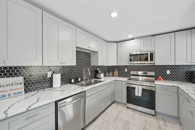 kitchen with sink, backsplash, light stone countertops, and appliances with stainless steel finishes