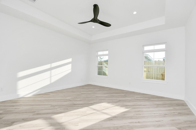 empty room featuring ceiling fan, a tray ceiling, and light hardwood / wood-style floors