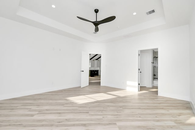 spare room with a raised ceiling, ceiling fan, and light wood-type flooring