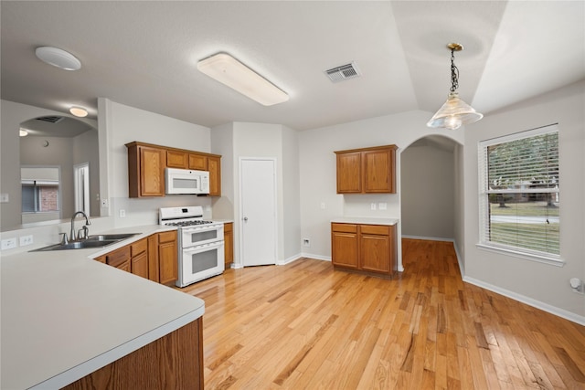 kitchen with arched walkways, white appliances, a sink, hanging light fixtures, and light countertops