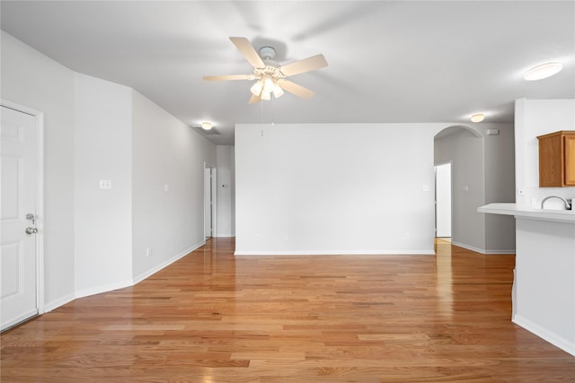 unfurnished living room with light wood-type flooring, ceiling fan, arched walkways, and baseboards