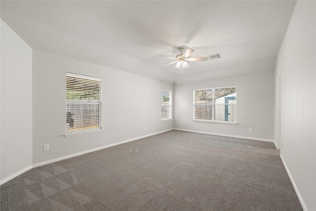 empty room featuring dark colored carpet, visible vents, ceiling fan, and baseboards