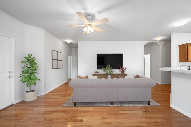 living room with light wood finished floors, baseboards, arched walkways, and a ceiling fan