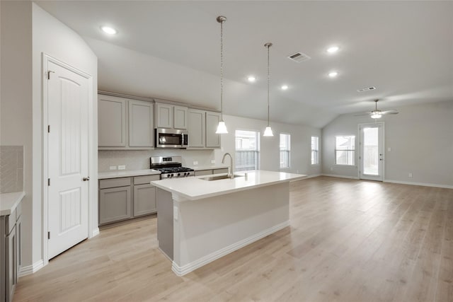 kitchen with lofted ceiling, sink, appliances with stainless steel finishes, gray cabinets, and a kitchen island with sink