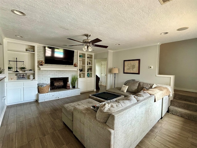 living room featuring crown molding, a brick fireplace, a textured ceiling, and built in shelves