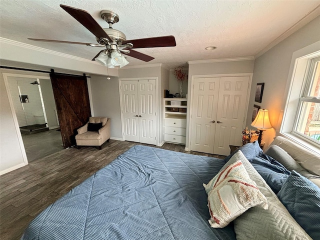 bedroom featuring dark hardwood / wood-style floors, ceiling fan, multiple closets, and a barn door