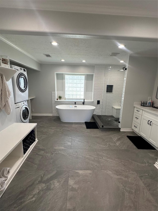 bathroom featuring shower with separate bathtub, stacked washer and dryer, vanity, ornamental molding, and a textured ceiling