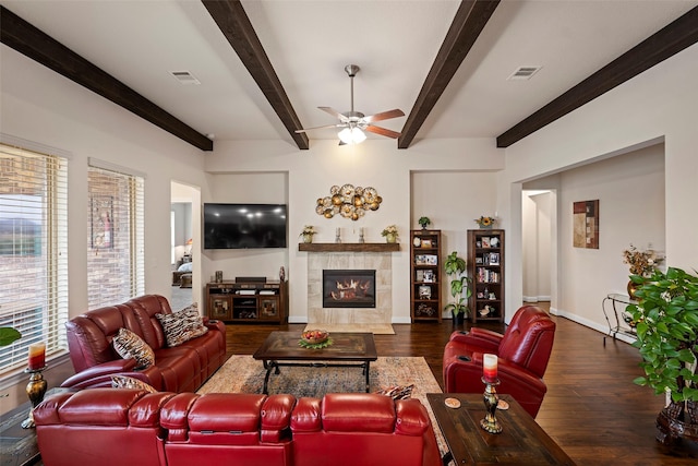 living room featuring ceiling fan, dark hardwood / wood-style flooring, beam ceiling, and a tile fireplace