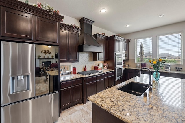 kitchen featuring premium range hood, sink, tasteful backsplash, appliances with stainless steel finishes, and light stone countertops