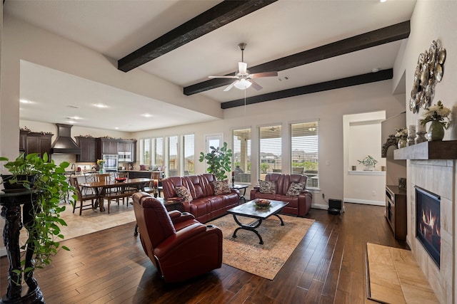 living room featuring ceiling fan, dark hardwood / wood-style floors, beam ceiling, and a tile fireplace