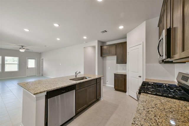 1312 Cypress Ln, Dayton, TX 77535 - kitchen with appliances with stainless steel finishes, ceiling fan, a center island with sink, light stone counters, and dark brown cabinetry