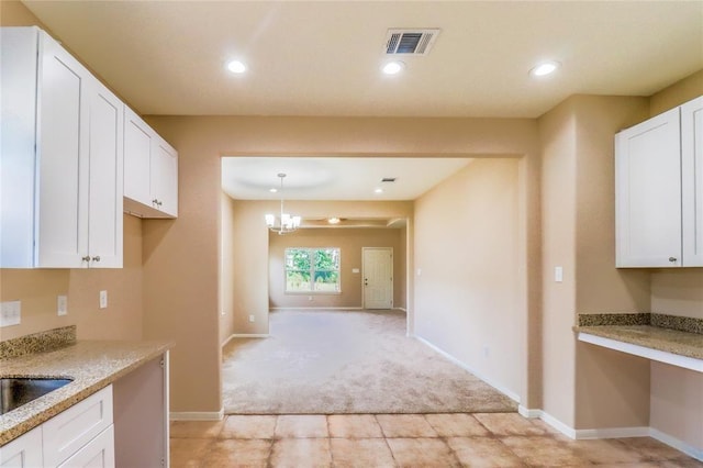 kitchen featuring decorative light fixtures, white cabinetry, light stone counters, light carpet, and an inviting chandelier