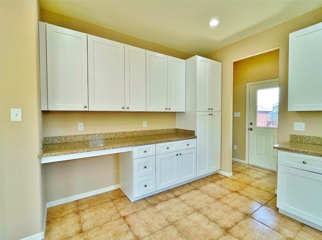 kitchen featuring built in desk, light stone countertops, and white cabinets