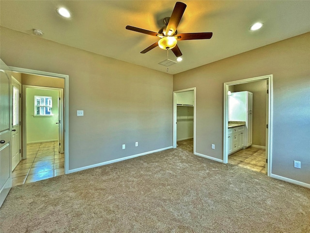 unfurnished bedroom featuring a walk in closet, light colored carpet, ceiling fan, ensuite bath, and a closet