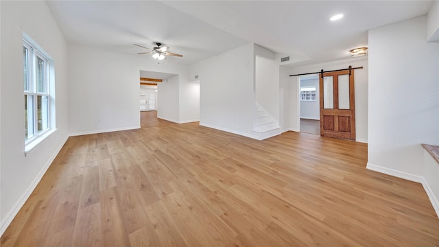 unfurnished living room featuring ceiling fan, plenty of natural light, a barn door, and light hardwood / wood-style flooring