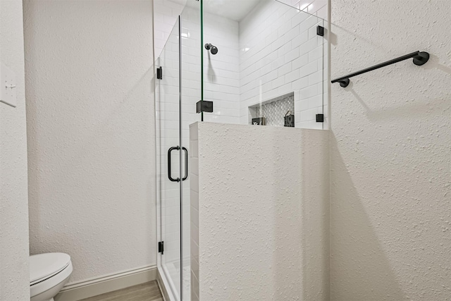 bathroom with hardwood / wood-style flooring, toilet, and a shower with door