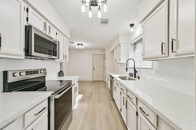 kitchen with sink, light hardwood / wood-style flooring, stainless steel appliances, light stone counters, and white cabinets