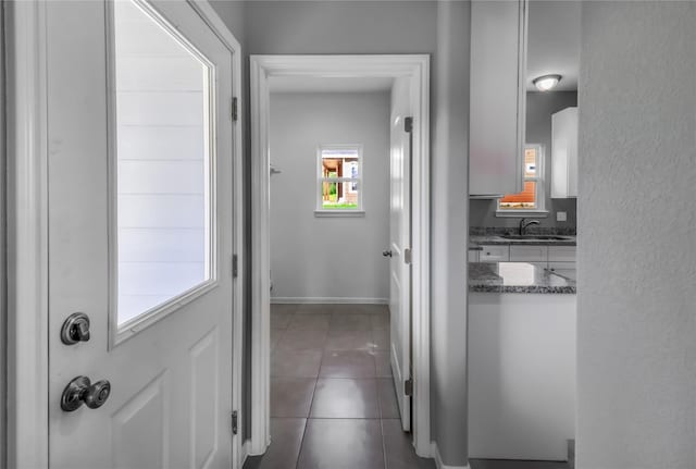 corridor featuring a sink, dark tile patterned floors, and baseboards