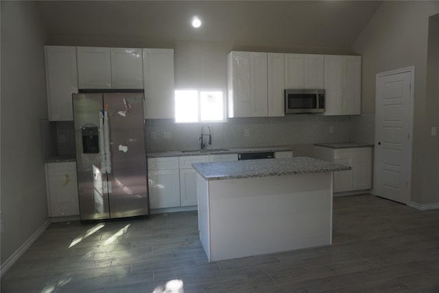 kitchen featuring sink, stainless steel appliances, light stone countertops, white cabinets, and a kitchen island