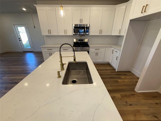 kitchen with light stone counters, appliances with stainless steel finishes, sink, and hanging light fixtures