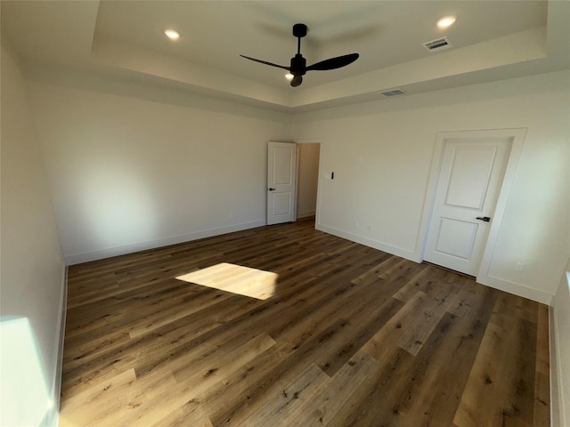 empty room featuring a tray ceiling, dark wood-type flooring, and ceiling fan