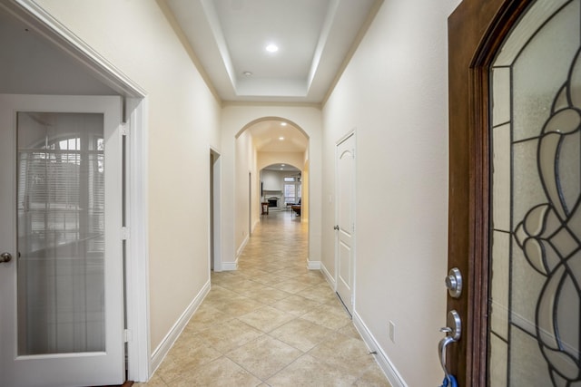 corridor with light tile patterned flooring and a tray ceiling