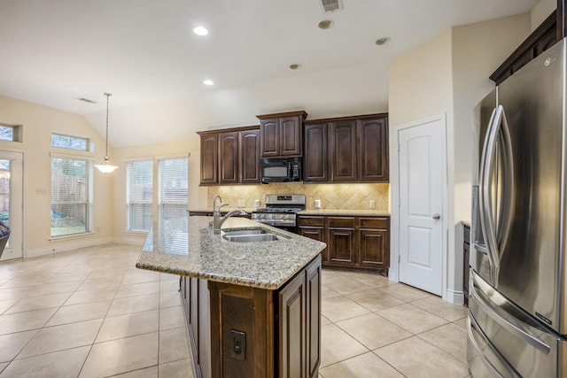 kitchen with lofted ceiling, light tile patterned floors, appliances with stainless steel finishes, a kitchen island with sink, and light stone counters