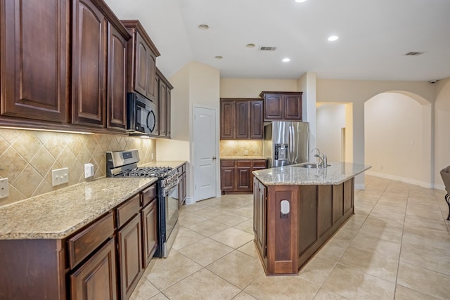 kitchen with sink, light stone counters, a center island with sink, light tile patterned floors, and appliances with stainless steel finishes