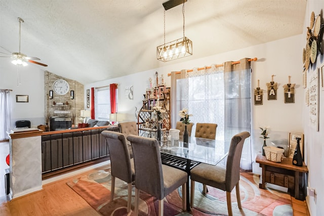 dining room with vaulted ceiling, a textured ceiling, hardwood / wood-style flooring, ceiling fan, and a fireplace