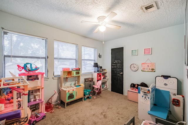 recreation room with a textured ceiling, light colored carpet, and ceiling fan