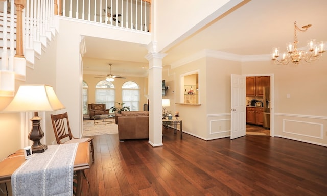 living room featuring ceiling fan with notable chandelier, ornamental molding, dark hardwood / wood-style flooring, and decorative columns