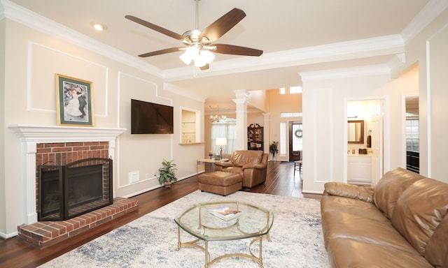 living room featuring dark wood-type flooring, ornamental molding, a fireplace, and ornate columns